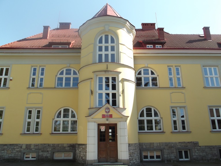 Dwukondygnacyjny budynek z żółtą elewacją i czerwoną dachówką. Centralnie umieszczona, cylindryczna klatka schodowa z wejściem. Okna półokrągłe i prostokątne. Dolna część elewacji z kamienną podmurówką.
